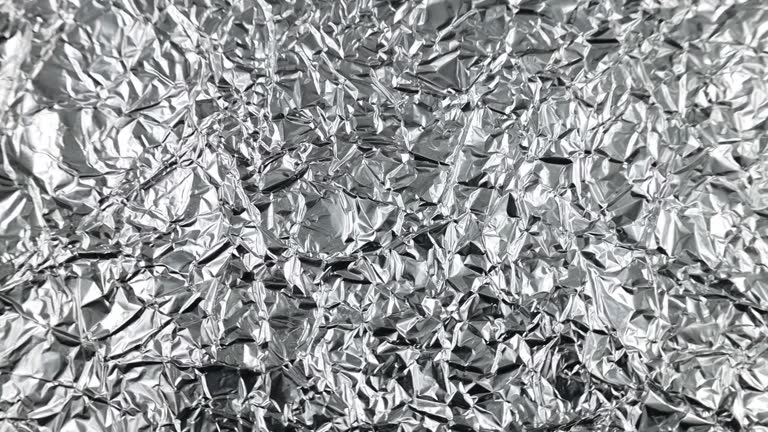 Wrinkled silver colored shiny aluminum foil texture circle rotation close up