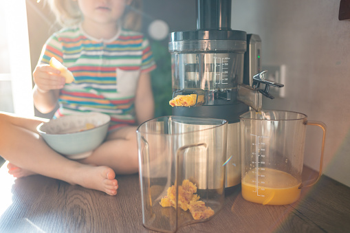 Little girl making fresh juice on the table in home kitchen. Focus on juicer. High quality photo