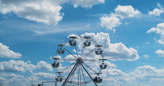 Small ferris wheel against a perfect blue sky with white clouds. Slow rotation, calm rest. High quality 4k footage