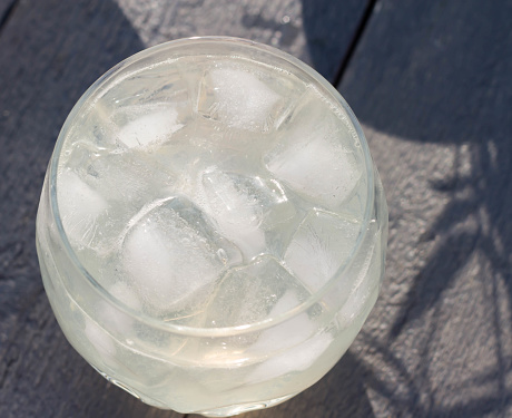 A glass of sparkling water and ice cubes on a gray wooden background. Top view. Sunny day.