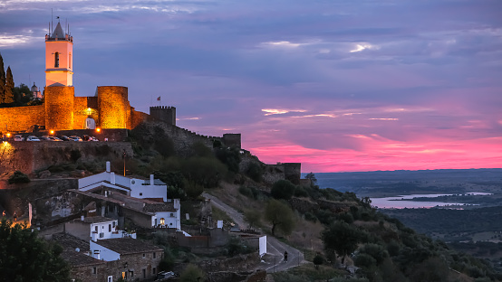 A multicolored beautiful sunset photo of Monsaraz castle.  The castle looks over a valley with water.   Second photo is a close up head and neck photo of an emu staring at the camera.