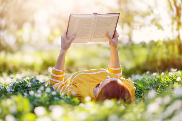 Woman lying on the blooming meadow and reading book. stock photo