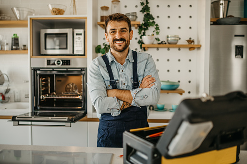 Portrait of a handsome handyman, plumber, or electrician working at a house with his tools and looking at the camera smiling - home improvement concepts