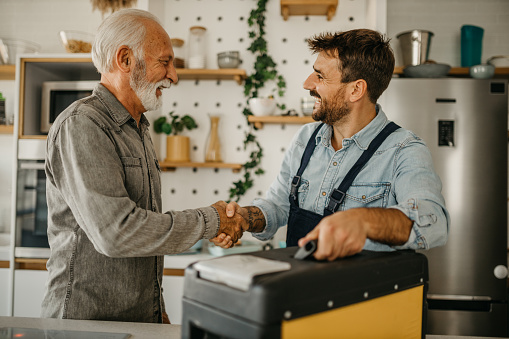 Happy senior shaking hands with a repairman. Home interior. Senior man welcoming the repairman.