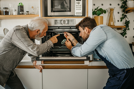 Senior man explaining to the technician of household maintenance service what is the issue in the kitchen oven.