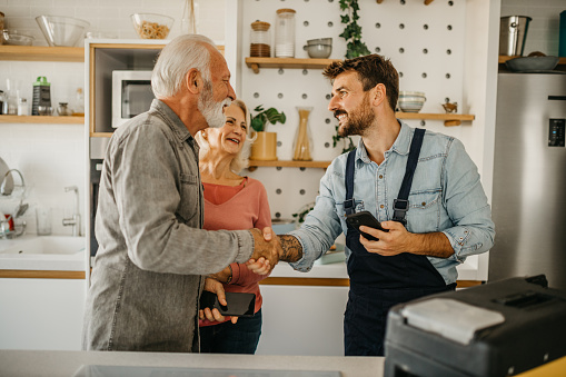 The repairman gives repair estimates to a senior couple and handshaking. Service Industry: Repairman works at customer's home.