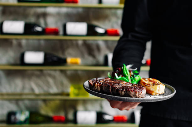 Un jeune beau chef en uniforme noir tient dans ses mains une viande de faux-filet de steak de bœuf prête - Photo