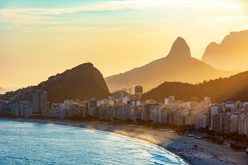 Sunset at Copacabana beach in Rio de Janeiro with the light coming from behind the buildings and hills