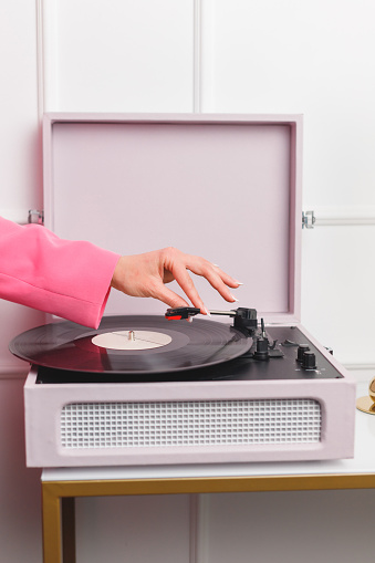 Female hand in pink blazer starting vinyl turntable at the home party