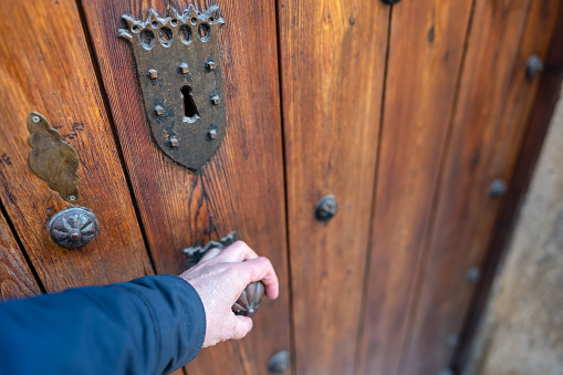 Man's hand opening a medieval wooden door in the old town of Pedraza, Segovia, Spain