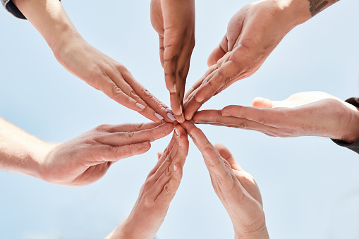 Blue sky, community and connection of hands in circle for friendship, support and collaboration outdoors. Diversity, love and group of people with fingers together for trust, motivation and mission