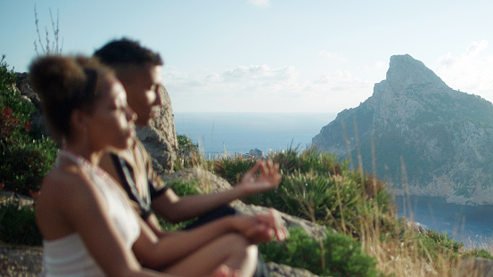 African ethnicity couple sitting in tranquility. Meditating on top of a mountain and looking down at the breathtaking mountain range