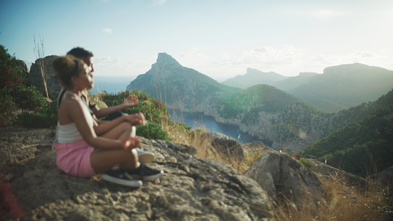 African ethnicity couple sitting in tranquility. Meditating on top of a mountain and looking down at the breathtaking mountain range