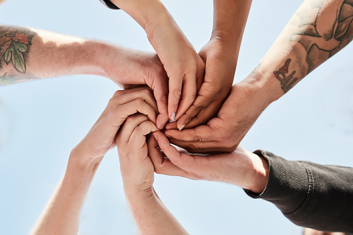 Hands, support and people in a unity circle for trust, love and connection with a blue sky background. Team building, diversity and hand of team outdoor in collaboration, community and togetherness.