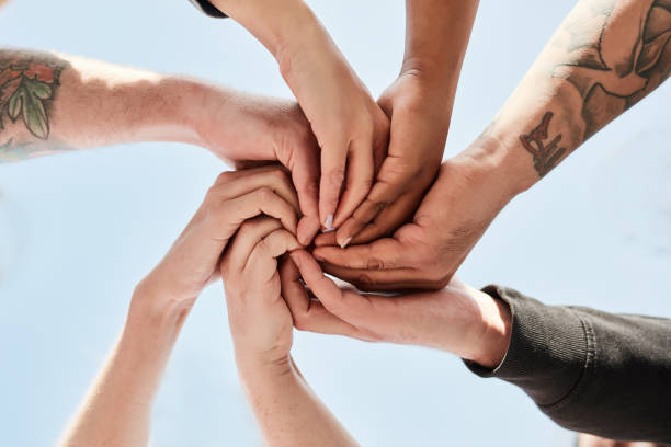 Hands, support and people in a unity circle for trust, love and connection with a blue sky background. Team building, diversity and hand of team outdoor in collaboration, community and togetherness. stock photo