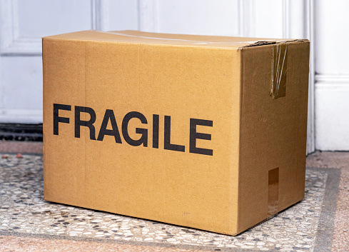 A deliver of a box with a large 'Fragile' sign, left in the front porch of a home.