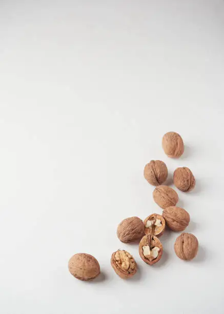 a handful of whole walnuts in shell and some halved with the nut inside scattered on a white surface with copy space
