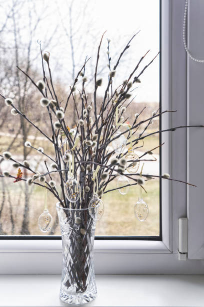 istock Crystal vase on windowsill with bunch of willow sprigs decorated for Easter with decorative glass Easter eggs, rustic style. 1464517396