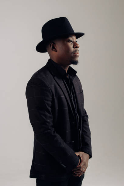 istock Young african man in suit and hat stands against gray background. 1464520470