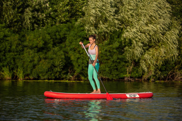 mujer atlética joven haciendo fitness en una tabla con un remo en un lago. - paddleboard oar women lake fotografías e imágenes de stock