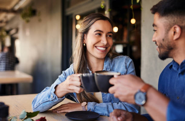 Cafe, couple date cheers and woman smile in a coffee shop with a man feeling love and happiness. Restaurant, discussion and happy people out for lunch talking about relationship with morning drink stock photo