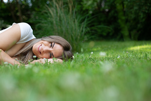 Portrait of a beautiful young blonde woman lying in green grass in the garden and looking at the camera