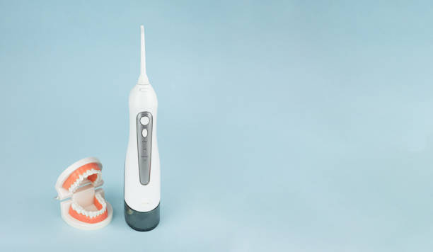 istock Dental prosthesis with oral cavity irrigator that cleans teeth on blue background, close-up. 1464529038
