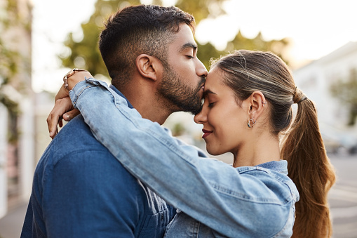 Couple, love and kiss forehead in city with face, romance and intimate relationship. Young man, kissing and hug happy woman in town for care, support and commitment on fun urban outdoor date together