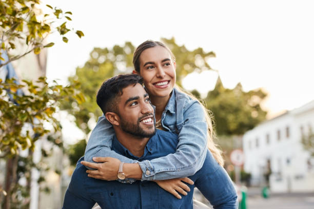 Travel, piggyback and happy couple with love in the city on a walk while on a romantic date. Happiness, smile and young man and woman having fun, walking and bonding in the town street on a vacation. stock photo