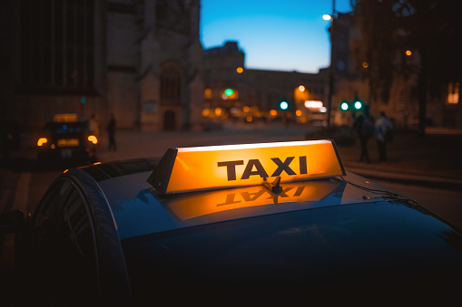 A close-up shot of a taxi sign in the warm colours of sunset with bokeh lights in the background. Urban transportation.
