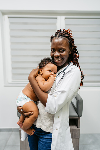 Portrait of a young black female pediatrician holding a newborn baby boy at the pediatric clinic.