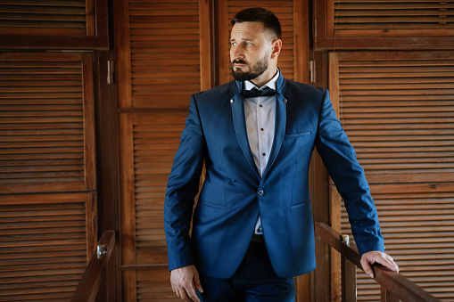 portrait of a groom with a beard in a blue suit and bow tie
