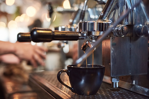 Cafe, barista and a coffee machine in the kitchen of a restaurant for beverage preparation or serving. Small business cup and pouring caffeine in a cafeteria using equipment for a latte or cappuccino