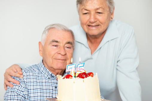 Senior couple with birthday cake on white background.