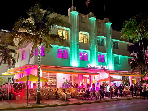 Miami beach, FL - USA, February 1, 2023. The Carlyle illuminated at night on Ocean drive, Miami Beach. The now condo building used to be a hotel built in 1939 epitomizes the art deco architecture of the time. Bright and colorful illumination lights the structure as well as cafe on the lowest floor and sidewalk.