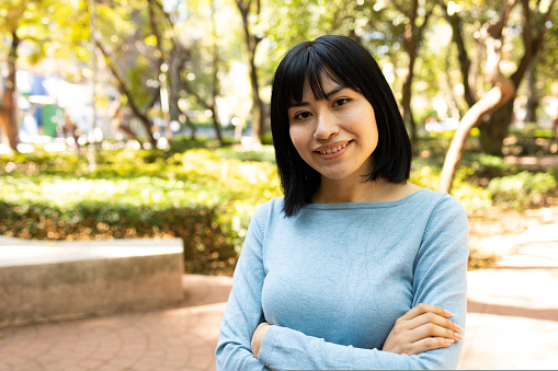 Portrait of young asian woman looking at camera and smiling outdoors. She have crossed arms. High quality photo