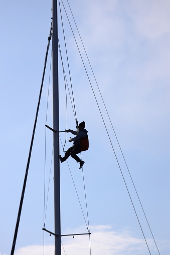 Bodrum,Mugla, Turkey. 15 January 2023: Young man hanging and repairs yacht mast