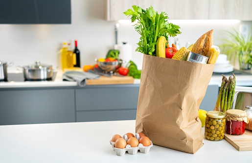 Close up view of a brown paper shopping bag full of groceries on kitchen counter. High resolution 42Mp indoors digital capture taken with SONY A7rII and Zeiss Batis 40mm F2.0 CF lens