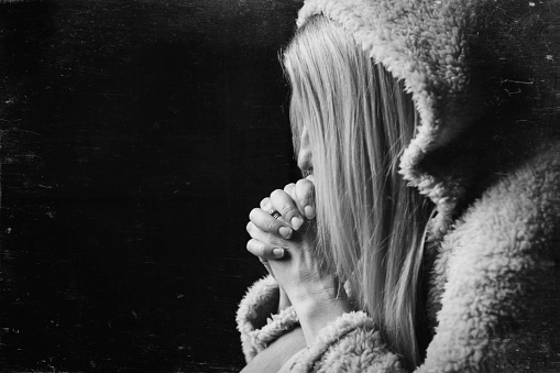 A black cand white image of a woman hidden by her hair in prayer.