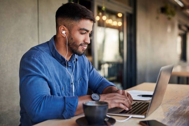 uomo, auricolari o laptop che digitano in un bar o in un ristorante per studiare all'università, al college o alla scuola con l'app podcast di apprendimento. musica per studenti, tecnologia o istruzione per la ricerca di laurea in campus remoto - university student laptop campus foto e immagini stock