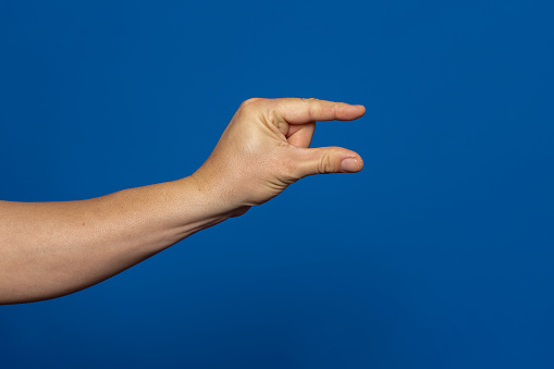 Male caucasian hand gesture of showing the small size with two fingers, isolated over the blue background.