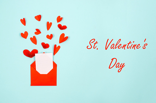 Empty white paper blank in red envelope and varios paper hearts on a blue background. Concept of the St. Valentine's day. Greeting card with place for text