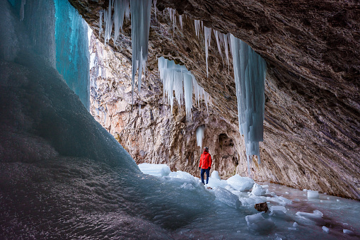 Hiker Exploring Frozen Ice Cave - Man in cave staring in wonder with icicles hanging down. Frozen ice cave outdoor adventure exploration.