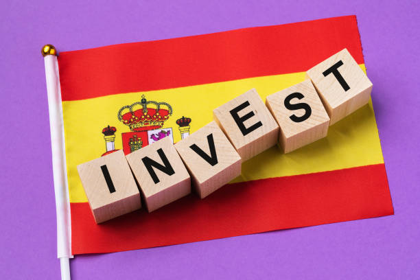 istock Wooden cubes with text and a flag on a colored background, a concept on the theme of investment in Spain 1464557523