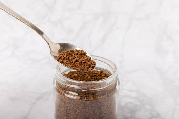 istock Instant coffee in a spoon and a glass jar on a white marble background. Place for text. Space for copy text 1464560923