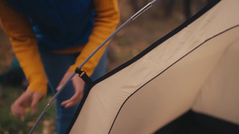 Young man and woman setting up camping tent in autumn forest, outdoor getaway