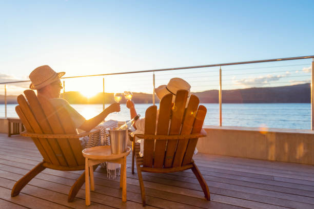 Couple relaxing and drinking wine and toasting on deck chairs Couple relaxing and drinking wine and toasting on deck chairs in an over water bungalow. They are looking at the view wealthy house stock pictures, royalty-free photos & images
