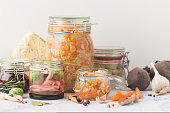 Glass jars with various pickled vegetables and ingredients on a marble background