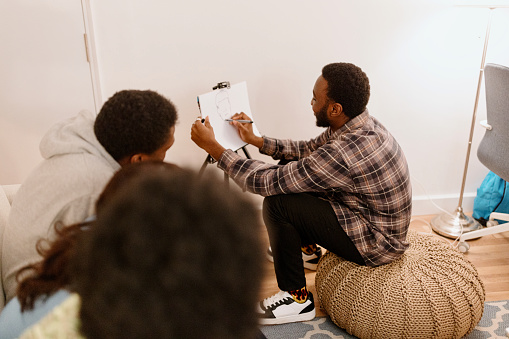 Young African American man drawing something on the paper for charades game. People have fun playing indoor games at home.