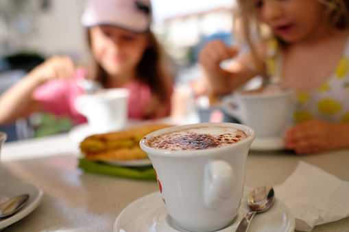 Family sightseeing trip in Florence, kids are enjoying their hot cacaos in local cafe while freshly prepared cappuccino is waiting to be tasted.